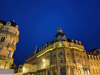 A very tall Hausmannian building with Christmas decorations displayed prominently on its upper baclony, capturing the urban landscape for the winter holidays