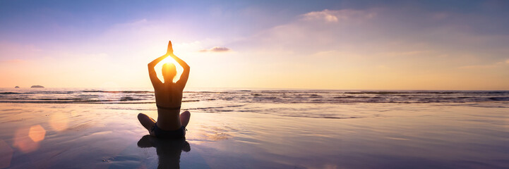 Wellbeing and mindfulness through yoga practice. Silhouette of a fit woman yogi in lotus pose on a...