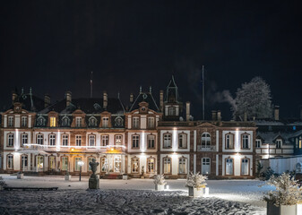 Snow-covered grounds of a majestic historical building illuminated under a clear night sky