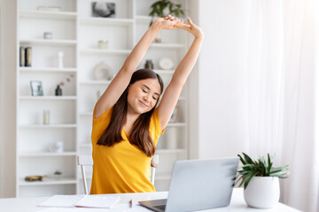 Fototapeta na wymiar Happy asian woman stretching with her arms raised, taking break at her home office