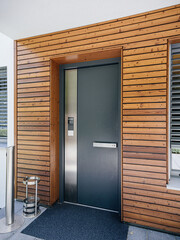 A modern wooden door with multiple secure points, accompanied by an interphone system and a CCTV camera on the left, exemplifying the security features of this property in the real estate market