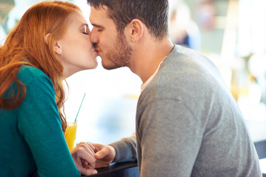 Couple, date and kiss with romance, coffee shop or restaurant with happiness together. Man, woman and love for relationship, care and smile for flirting on break for relax or bonding in cafe