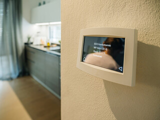 Modern smart home thermostat displaying temperature settings on a wall with blurred kitchen...