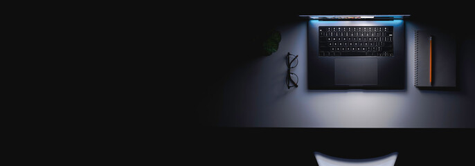 Laptop with a glowing screen on a table in the dark, top view, copy space.