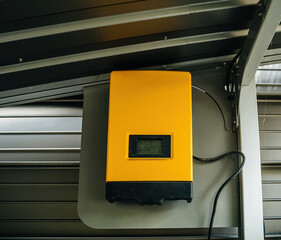Industrial yellow solar power inverter installed on a metal wall.