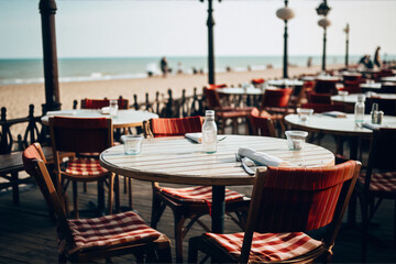 Naklejka premium An empty restaurant table with a water bottle and glass on the beach with a blurred background of the ocean and a few people walking.