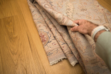 A close-up view of a hand revealing an intricate pattern on an antique rug laid upon a polished...