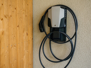 Wall-mounted electric vehicle charger next to a wooden facade, highlighting the integration of...