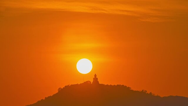 Time Lapse The sun circles behind the Buddha on the mountain as the sun travels from the sky and falls behind the mountain. .The Sky gradually changed color from yellow to orange and red over time.