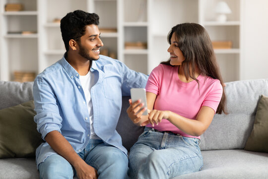 Hindu couple on couch sharing phone, both smiling