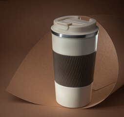 beige thermo cup or thermos mug for tea or coffee on brown background. Hot beverage.