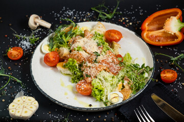 Classic Caesar salad with salmon. On a black stone background. In a plate, close-up.