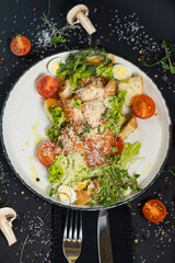 Classic Caesar salad with salmon. On a black stone background. In a plate, close-up.