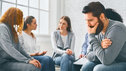 Depressed man sitting at rehab group therapy