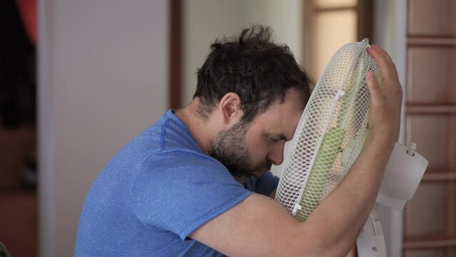 Man Enjoying Cool Wind From Electric Fan at Home at Summer Day. Male Suffer From Heat High Temperature in Front of Ventilator Cooling Herself With Electric Fan-Cooler. Hot Heat Day, Climate Change.