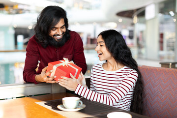 Loving indian guy giving his girlfriend birthday gift at cafe