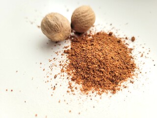 Two whole nutmegs and powder on bright background.