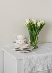 A bouquet of tulips in a glass vase and retro-style ceramic tableware on a white chest of drawers