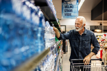 Senior bearded happy male purchasing a bottle of water. Man buying bottled water in grocery store.