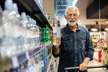 Happy mature man shopping in supermarket chooses water. Senior happy male shopping in supermarket...