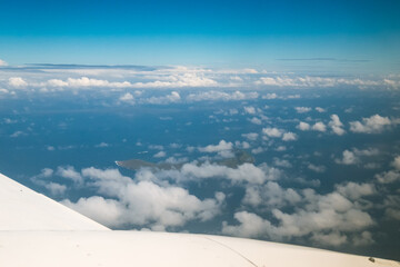 A plane is flying over the ocean with clouds in the sky