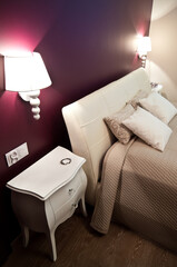 Detail of an elegant bedroom of a modern home with beige pillows and bedding and classic look lamps on deep red color walls