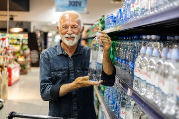Happy mature man shopping in supermarket chooses water. Senior happy male shopping in supermarket chooses water.