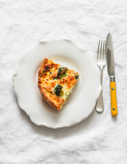 A piece of quiche with broccoli, chicken, spinach and cheese on a light background, top view