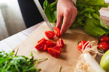 A close up of girl's or woman's hands peeling and cutting vegetables with knife making salad	
