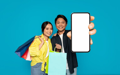 A smiling man and woman, carrying colorful shopping bags, cheerfully present a smartphone with a blank screen - 762379113