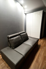 Modern bedroom, simplistic style with brown leather sofa and wall lighting. Contemporary youth room design.