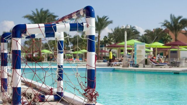 Gates for playing water polo near outdoor pool in hotel against backdrop of relaxation areas on sunny day, active recreation in pool