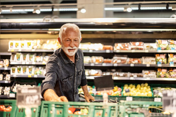 Mature man shopping for fruit And vegetables in a supermarket. Man defining quality of tomato in...