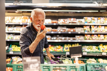 Mature man shopping for fruit And vegetables in a supermarket. Man defining quality of tomato in...