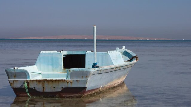 Abandoned fishing boat stranded in ocean, destroyed boat against the red sea horizon in Egypt