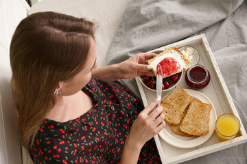Young woman having breakfast in bed buttering toasted bread - 762385525