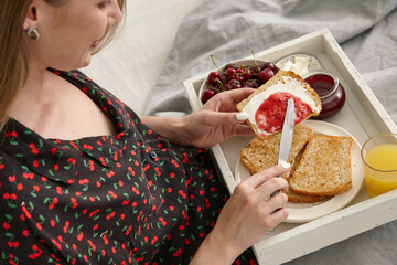 Young woman having breakfast in bed buttering toasted bread - 762385578