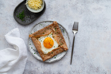 Homemade buckwheat crepes. Galettes Bretonnes with cheese and fried egg on a grey background. Traditional French cuisine.