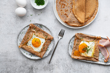 Homemade buckwheat crepes. Galettes Bretonnes with cheese and fried egg on a grey background. Traditional French cuisine.