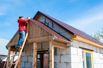 A worker builds a roof in a house while standing on a wooden ladder. Blue sky - 762395120