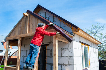 A worker builds a roof in a house while standing on a wooden ladder. Blue sky - 762396733