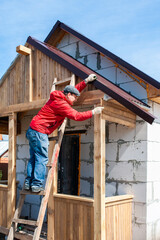 A worker builds a roof in a house while standing on a wooden ladder. Blue sky - 762396927