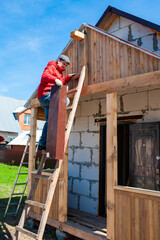 A worker builds a roof in a house while standing on a wooden ladder. Blue sky - 762406359