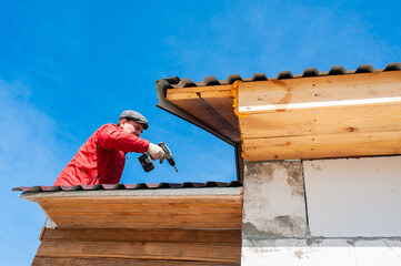 A worker builds a roof in a house while standing on a wooden ladder. Blue sky - 762406937