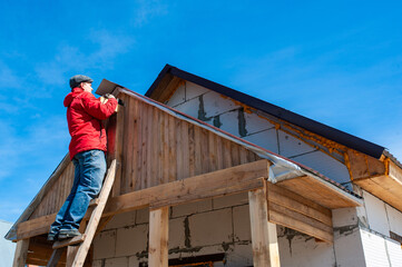 A worker builds a roof in a house while standing on a wooden ladder. Blue sky - 762407342