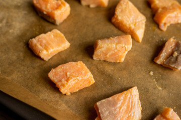 Close-up of raw fresh salmon fillets cut into cubes and arranged on parchment paper in a tray, ready for cooking, showcasing their quality and freshness