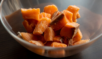  Close-up of raw fresh salmon fillets cut into cubes and presented in a glass bowl, highlighting...
