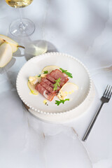 Summer pear salad with prosciutto, arugula on light great marble background. Healthy diet concept. Italian cuisine. Vertical