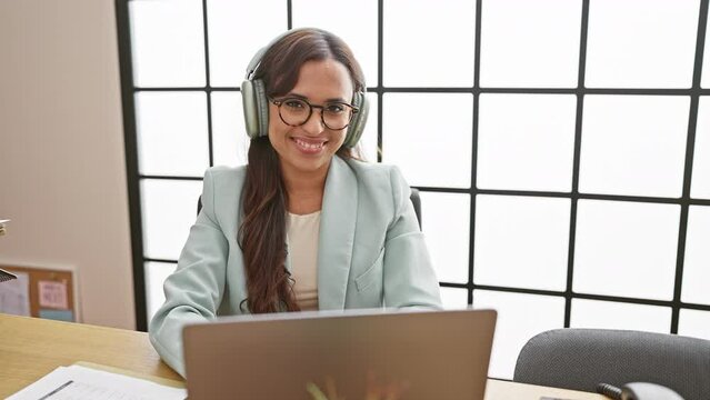 Young beautiful hispanic woman business worker using laptop and headphones working at the office