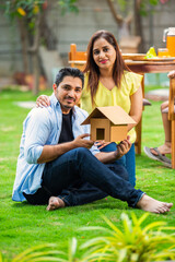 Real estate and India - couple holding house model while sitting in the lawn